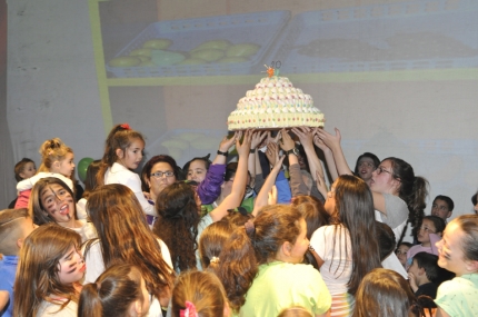 Niños y niñas de la ludoteca sujetan la gran tarta de chuches del 20 cumpleaños. 