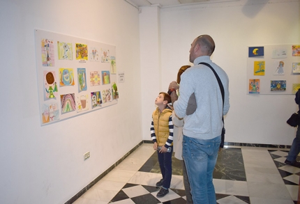 El pequeño, Pablo Baena, ganador del concurso, mira los dibujos de la muestra junto a sus padres.