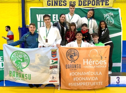 Delegación de deportistas del Club Baransu en el torneo de Gines posan con los colores del club y la pancarta de la asociación Héroes hasta la Médula