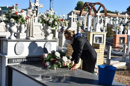 Una mujer limpia la lápìda de sus familiares con mascarilla 