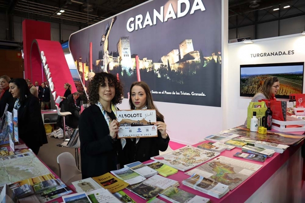 Dos agentes turísticas enseñan un calendario de Albolote en el stand de Granada. Abajo, representantes del Ayuntamiento de Albolote con el alcalde Salustiano Ureña a la cabeza.